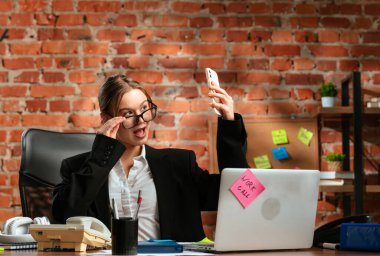 Ofis ortamındaki bir iş kadını akıllı telefonuyla eğlenceli bir selfie çeker, kendine güvenini ve neşesini ifade eder..