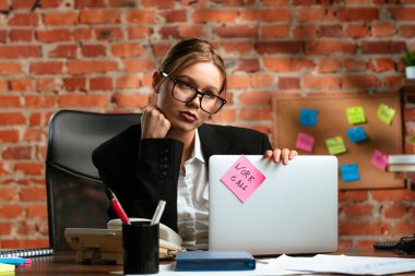 Gözlüklü bir iş kadını elinde bir dizüstü bilgisayarla duvarın arkasında 