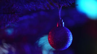 Bir çam ağacının dalında asılı, ışıltılı bir Noel süsü, festival ışıklarıyla çevrili. Mutlu Noeller ve mutlu yıllar kavramı..