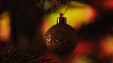 Bir çam ağacının dalında asılı, ışıltılı bir Noel süsü, festival ışıklarıyla çevrili. Mutlu Noeller ve mutlu yıllar kavramı..