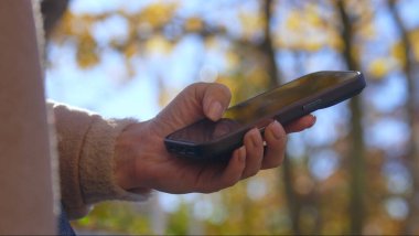 Bulanık bir sonbahar ormanı arka planına sahip akıllı bir telefonu tutarak, sakin bir açık hava anını yakalıyorum..