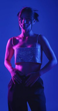 Genç bir Koreli model stüdyoda poz veriyor. Bir kadın kendine güvenerek duruyor, parlak bir bluz giyiyor, çarpıcı mavi ve pembe neon ışıklarla aydınlanıyor..