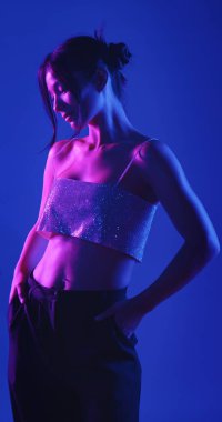 Genç bir Koreli model stüdyoda poz veriyor. Bir kadın kendine güvenerek duruyor, parlak bir bluz giyiyor, çarpıcı mavi ve pembe neon ışıklarla aydınlanıyor..