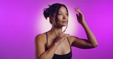 Genç bir Koreli model, pembe neon ışıklarla aydınlatılmış bir stüdyoda poz veriyor. Konsept güzellik, moda ve doğal kadınsı güzellik..