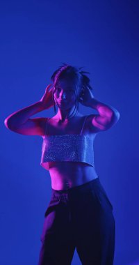 Genç bir Koreli model stüdyoda poz veriyor. Bir kadın kendine güvenerek duruyor, parlak bir bluz giyiyor, çarpıcı mavi ve pembe neon ışıklarla aydınlanıyor..