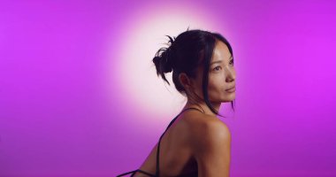 Genç bir Koreli model, pembe neon ışıklarla aydınlatılmış bir stüdyoda poz veriyor. Konsept güzellik, moda ve doğal kadınsı güzellik. Yan görünüm.
