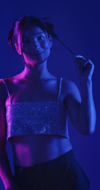 Genç bir Koreli model stüdyoda poz veriyor. Parlak bir bluz giyen bir kadın, çarpıcı mavi ve pembe neon ışıklarla aydınlatılır..