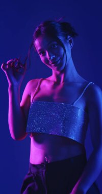 Genç bir Koreli model stüdyoda poz veriyor. Parlak bir bluz giyen bir kadın, çarpıcı mavi ve pembe neon ışıklarla aydınlatılır..