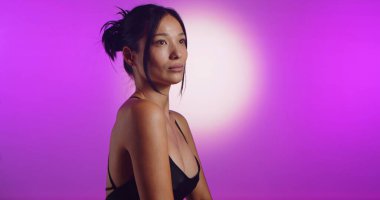 Genç bir Koreli model, pembe neon ışıklarla aydınlatılmış bir stüdyoda poz veriyor. Konsept güzellik, moda ve doğal kadınsı güzellik..