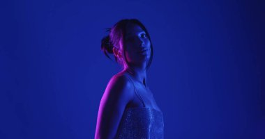 Genç bir Koreli model stüdyoda poz veriyor. Parlak bir bluz giyen bir kadın, çarpıcı mavi ve pembe neon ışıklarla aydınlatılır..