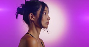 Genç bir Koreli model, pembe neon ışıklarla aydınlatılmış bir stüdyoda poz veriyor. Konsept güzellik, moda ve doğal kadınsı güzellik. Yan görünüm.