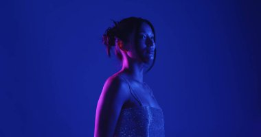 Genç bir Koreli model stüdyoda poz veriyor. Parlak bir bluz giyen bir kadın, çarpıcı mavi ve pembe neon ışıklarla aydınlatılır..