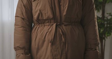 Sıcak ve tarz için tasarlanmış, kemerli bir bele sahip kahverengi bir kışlık ceket ayrıntılı bir görünüm.