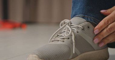 Modern gri spor ayakkabısının bağcıklarını bağlayan bir elin detaylı görüntüsü, günlük aktiviteleri vurguluyor..