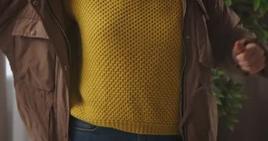 Kapalı bir yerde kahverengi kışlık ceket giyen, sarı desenli örülü süveter giyen bir kadının yakın çekimi. Yavaş çekim.