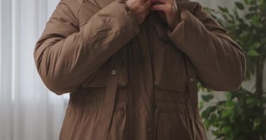Dışarı çıkmaya hazırlanırken kahverengi yalıtımlı ceketinin düğmelerini ilikleyen bir kadının ellerine yaklaş. Yavaş çekim.