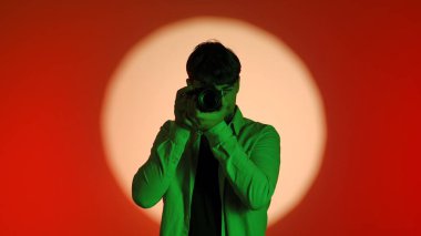 Sahne arkasında yeşil tişörtlü bir fotoğrafçıyla birlikte parlak bir ışık çemberiyle kırmızı bir arkaplan karşısında fotoğraf çekiyor..