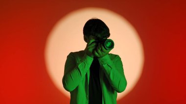 Sahne arkasında yeşil tişörtlü bir fotoğrafçıyla birlikte parlak bir ışık çemberiyle kırmızı bir arkaplan karşısında fotoğraf çekiyor..