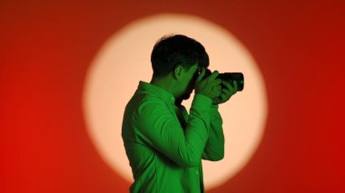 Sahne arkasında yeşil tişörtlü bir fotoğrafçıyla birlikte parlak bir ışık çemberiyle kırmızı bir arkaplan karşısında fotoğraf çekiyor..