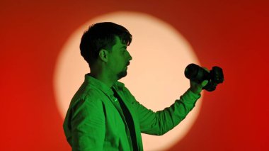 Sahne arkasında yeşil tişörtlü bir fotoğrafçıyla birlikte parlak bir ışık çemberiyle kırmızı bir arkaplan karşısında fotoğraf çekiyor..