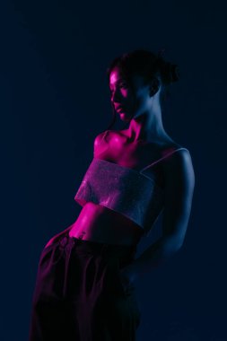 Genç bir Koreli model stüdyoda poz veriyor. Bir kadın kendine güvenerek duruyor, parlak bir bluz giyiyor, çarpıcı mavi ve pembe neon ışıklarla aydınlanıyor..