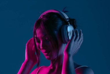 Kulaklık takan, müziğe dalmış bir kadın canlı mor ve mavi neon ışıklarla aydınlatılır..