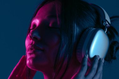Kulaklık takan, müziğe dalmış bir kadın canlı mor ve mavi neon ışıklarla aydınlatılır..