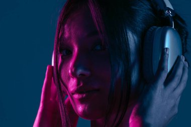 Kulaklık takan, müziğe dalmış bir kadın canlı mor ve mavi neon ışıklarla aydınlatılır..