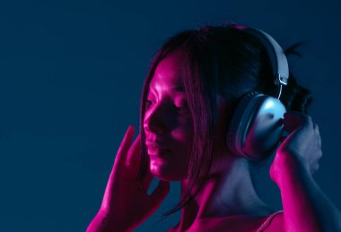 Kulaklık takan, müziğe dalmış bir kadın canlı mor ve mavi neon ışıklarla aydınlatılır..