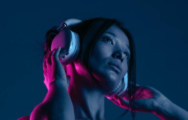 Kulaklık takan, müziğe dalmış bir kadın canlı mor ve mavi neon ışıklarla aydınlatılır..