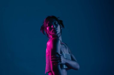 Genç bir Koreli model stüdyoda poz veriyor. Parlak bir bluz giyen bir kadın, çarpıcı mavi ve pembe neon ışıklarla aydınlatılır..