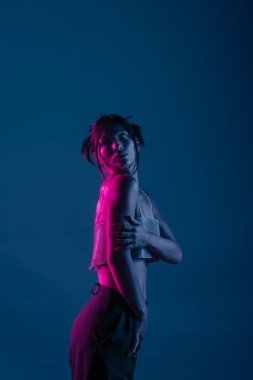 Genç bir Koreli model stüdyoda poz veriyor. Parlak bir bluz giyen bir kadın, çarpıcı mavi ve pembe neon ışıklarla aydınlatılır..