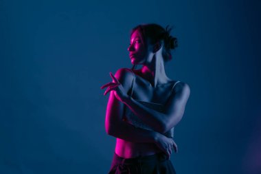 Genç bir Koreli model stüdyoda poz veriyor. Parlak bir bluz giyen bir kadın, çarpıcı mavi ve pembe neon ışıklarla aydınlatılır..