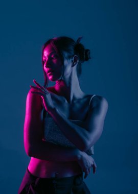 Genç bir Koreli model stüdyoda poz veriyor. Parlak bir bluz giyen bir kadın, çarpıcı mavi ve pembe neon ışıklarla aydınlatılır..