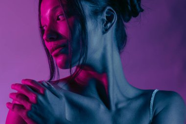 Genç bir Koreli model stüdyoda poz veriyor. Mor ve pembe neon ışıklarla aydınlatılmış bir kadın. Renkli güzellik, moda ve doğal kadınsı güzellik..