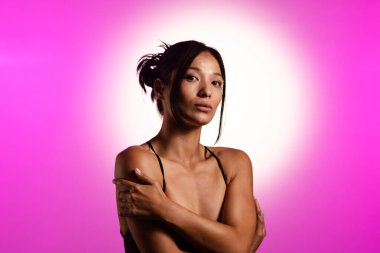 Genç bir Koreli model, pembe neon ışıklarla aydınlatılmış bir stüdyoda poz veriyor. Konsept güzellik, moda ve doğal kadınsı güzellik..