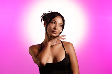 Genç bir Koreli model, pembe neon ışıklarla aydınlatılmış bir stüdyoda poz veriyor. Konsept güzellik, moda ve doğal kadınsı güzellik..