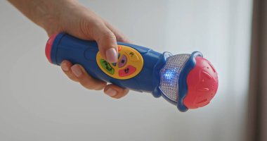 Parlak, renkli bir mikrofonu tutan bir elin yakın çekimi. Işıklı düğmeleri ve parlayan bir ışığı var..