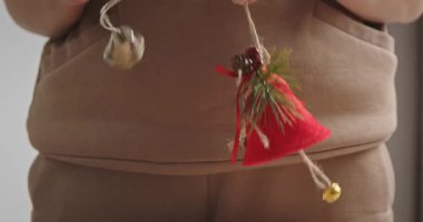 Dekoratif bir Noel çanını küçük reklam müzikleri ve bayram süsleriyle tutup sallayan bir kadının neşeli bir ses çıkarması. Yavaş çekim.