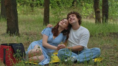 Yeşilliklerle çevrili yemyeşil bir ormanda piknik yaparken huzurlu bir anın tadını çıkaran genç bir çift..