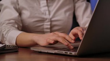 Bir dizüstü bilgisayarın klavyesine yazı yazan, bir iş yeri senaryosu tasvir eden yakın çekim elleri.