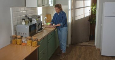 Gündelik giysiler içinde genç bir kadın parlak, modern bir mutfakta bambu bir hasırı açıyor. Günlük rutin, yaşam tarzı.