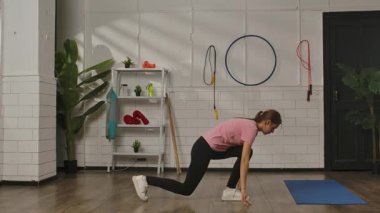 Pembe gömlekli ve siyah taytlı bir kadın spor salonunun ahşap zemininde hamlesini yapıyor. Egzersiz, kadınlar için fitness eğitimi, sağlıklı yaşam tarzı..