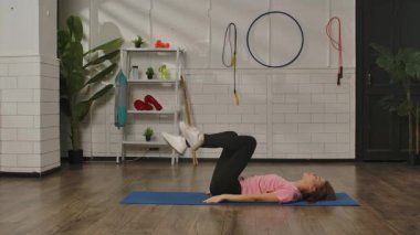 Spor kıyafetli bir kadın spor salonunda çeşitli ekipmanlarla mavi bir minder üzerinde egzersiz yapıyor. Kadın bisiklet bacak egzersizi yapıyor. Egzersiz, kadınlar için fitness eğitimi, sağlıklı yaşam tarzı..