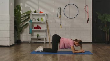 Evde spor salonundaki mavi bir paspasın üzerinde ekipman ve bitkilerle spor yapan bir kadın. Egzersiz, kadınlar için fitness eğitimi, sağlıklı yaşam tarzı..