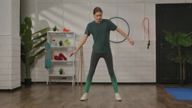 Genç bir kadın spor salonunda spor aletleri ve bitkilerle yan yana geriniyor. Kadın gövde bükümü yapıyor..