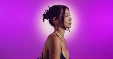 Genç bir Koreli model, pembe neon ışıklarla aydınlatılmış bir stüdyoda poz veriyor. Konsept güzellik, moda ve doğal kadınsı güzellik. Yavaş çekim.