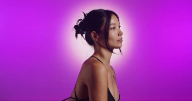 Genç bir Koreli model, pembe neon ışıklarla aydınlatılmış bir stüdyoda poz veriyor. Konsept güzellik, moda ve doğal kadınsı güzellik. Yavaş çekim.