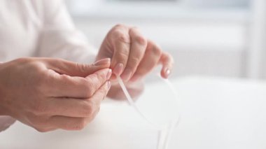 Manikürlü tırnaklarıyla beyaz bir kablo bağı tutan, düzgün ve düzenli bir yaşam tarzını ön plana çıkaran eller..