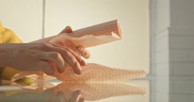 Sarı bir kazakla ellerini kapat ve cam bir yüzey üzerindeki dokuma rulosundan turuncu bir mutfak havlusunu parçala..